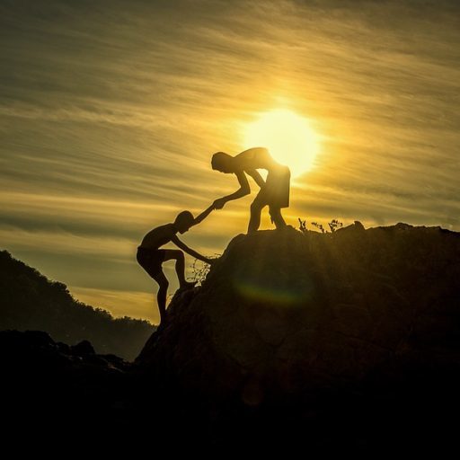 Silhouette of one person helping another up a rock at sunset